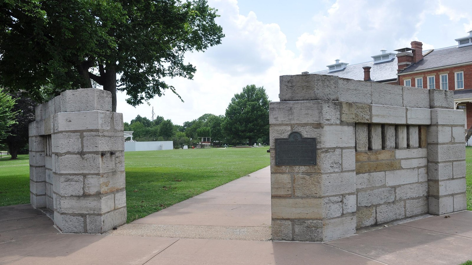 A wide sidewalk separates two segments of gray roughhewn stone wall 9 feet tall 2 feet thick.