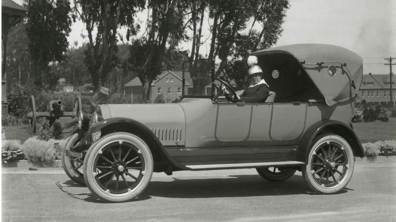 Black and white photograph of a women sits at the driver seat of an automobile. 