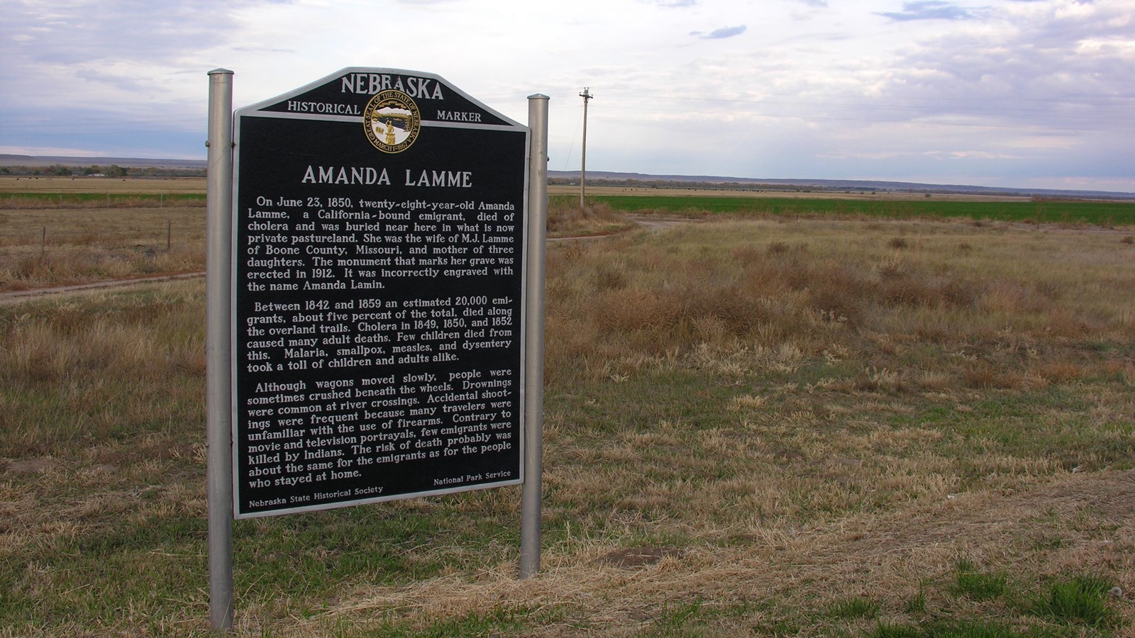 A large interpretive sign about Amanda Lamme stands on a grass field with cloudy sky above.