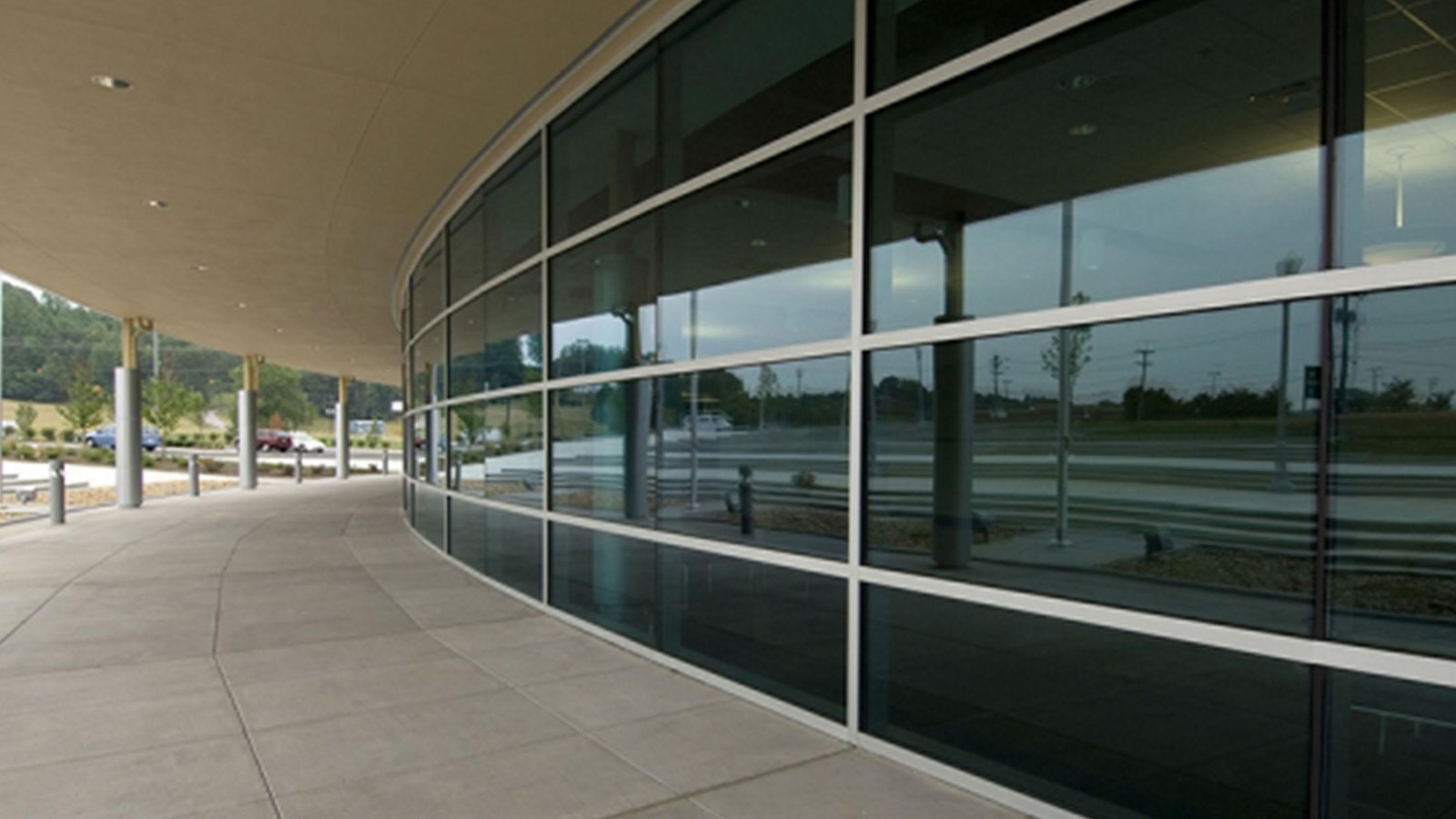 A glass-fronted building under an overhang with adjacent parking lot