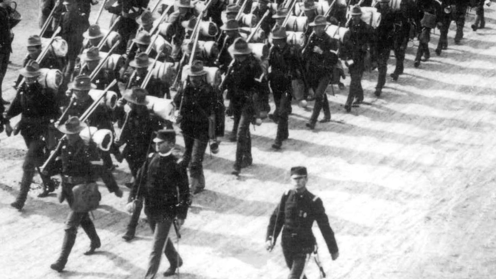Black and white photograph of soldiers marching through a large gate, heading off to war.