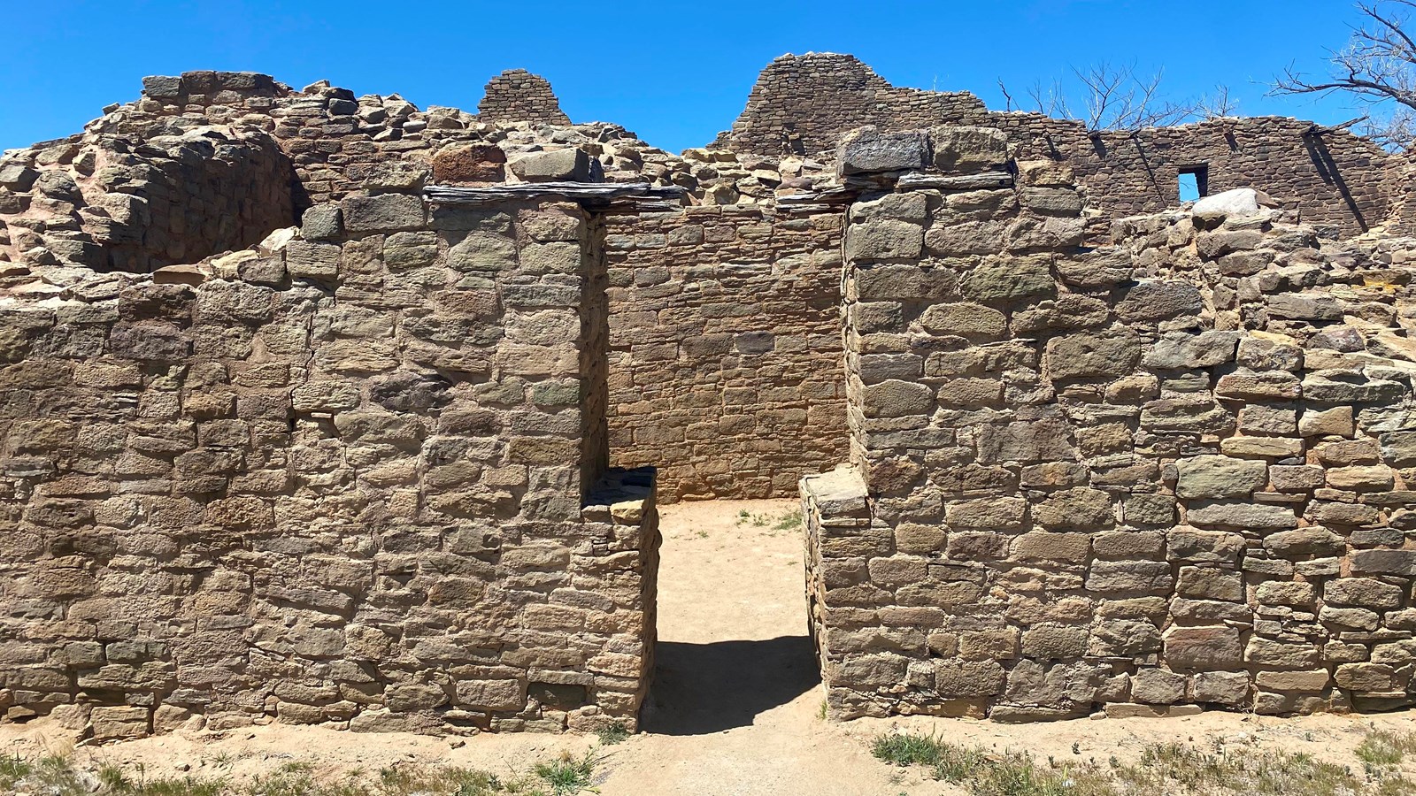 A T shaped door to an open room with sandstone walls under a blue sky.
