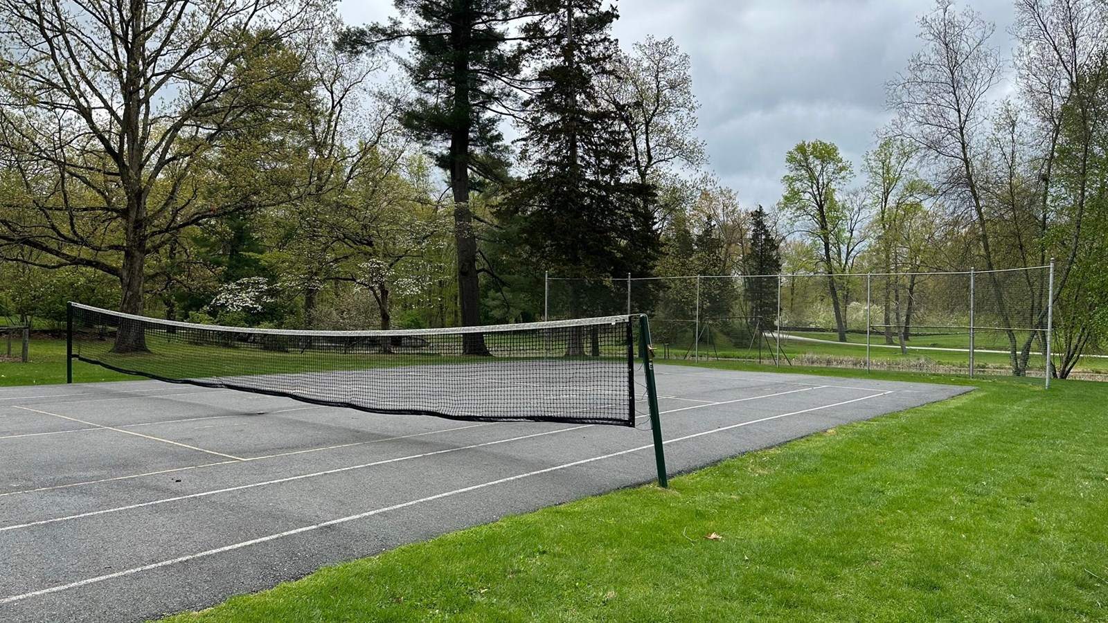 An asphalt tennis court with wire back drops on each end.