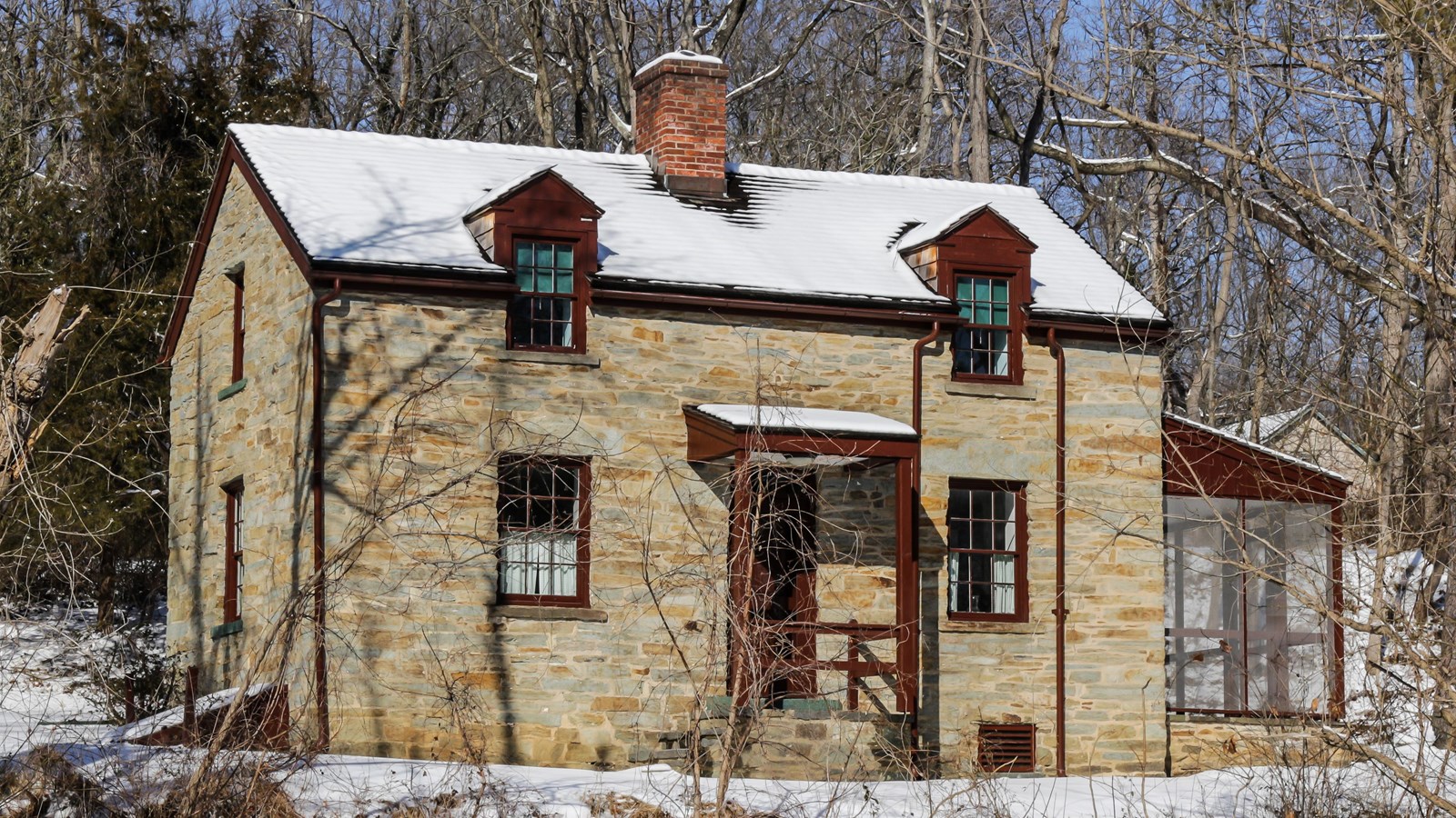 A tan lockhouse sits with snow on the roof.