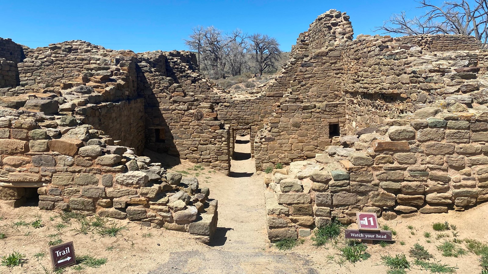 A downward sloping trail entering into a series of sandstone walled rooms with caution signs.
