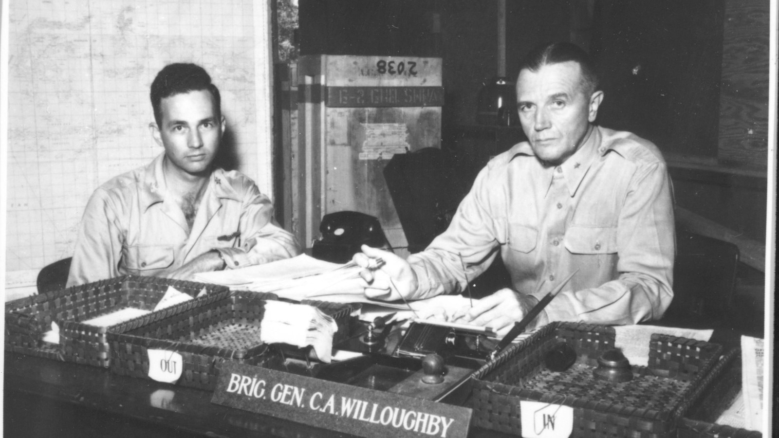 Black-and-white photograph of two men in military uniforms sitting at a desk in an office.