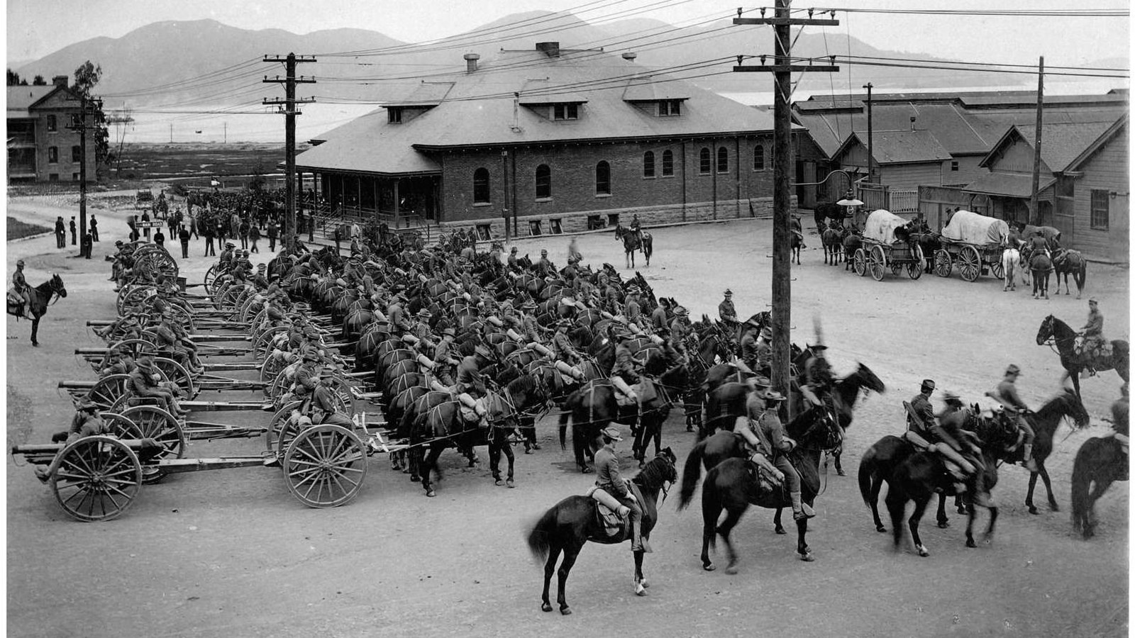 Black and white photo of Several rows of men on horseback. The rear row is pulling artillery.