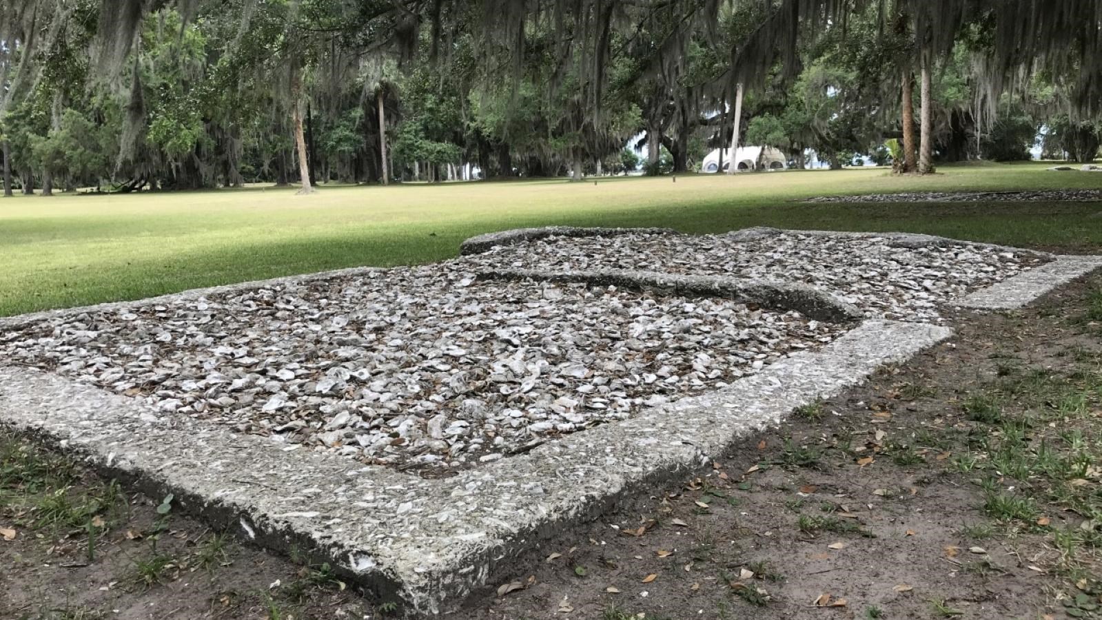 A tabby house foundation is surrounded by grassy area and live oak trees overhead.