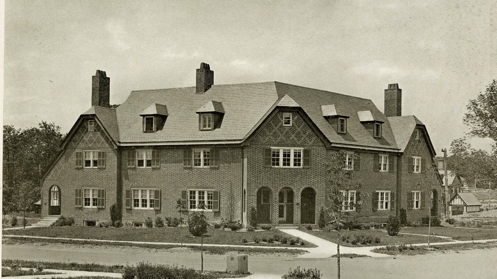 Black and white of large home with grass and shrubs in front and sidewalk leading away on both sides