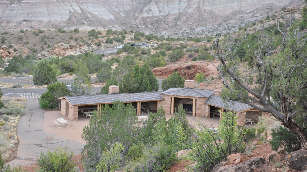 Stone structure with open walls covering picnic tables, in an open area surrounded by canyon walls