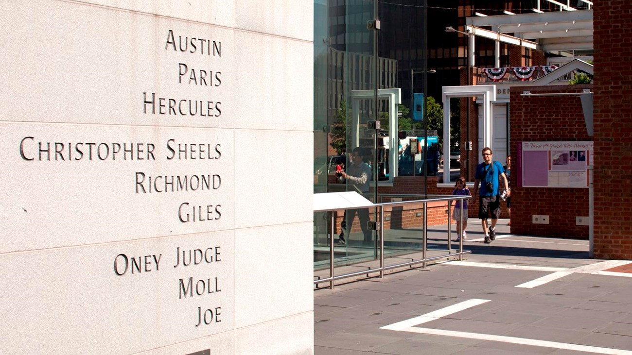 Photo of an outdoor exhibit featuring nine names engraved on a freestanding wall.