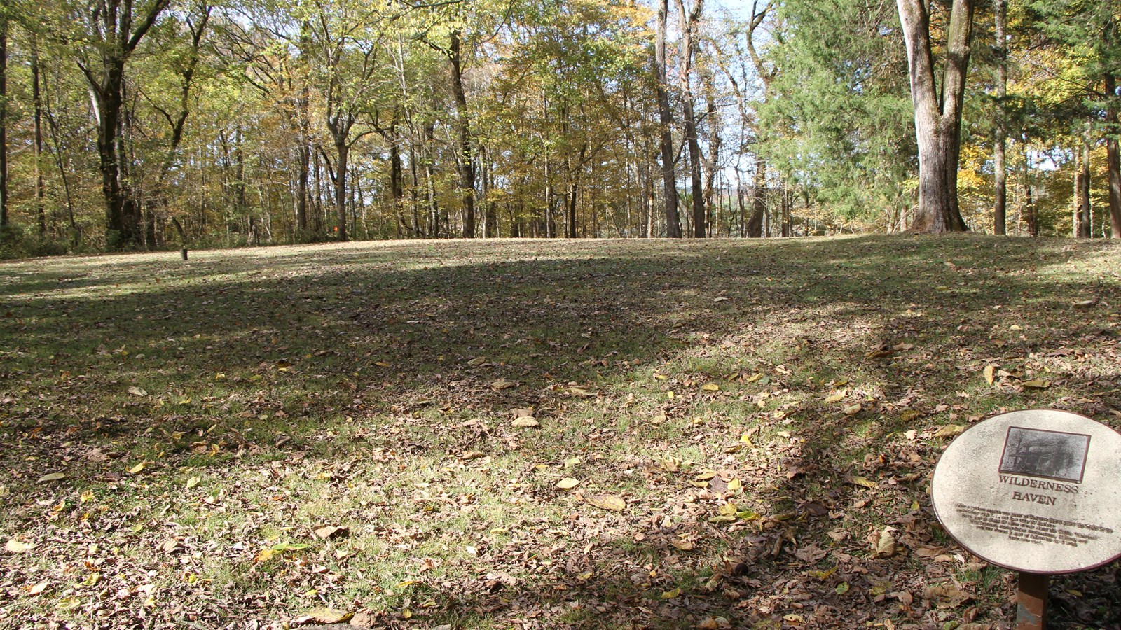 Small round sign titled “Wilderness Haven” is to the right, open space surrounded by trees where hou