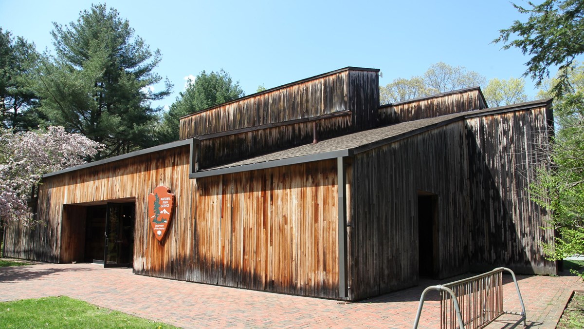 A wooden visitor center with large windows in front and brick sidewalk surrounding.