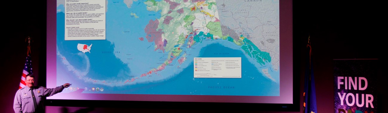 A ranger points to a large map of Alaska on a projector screen