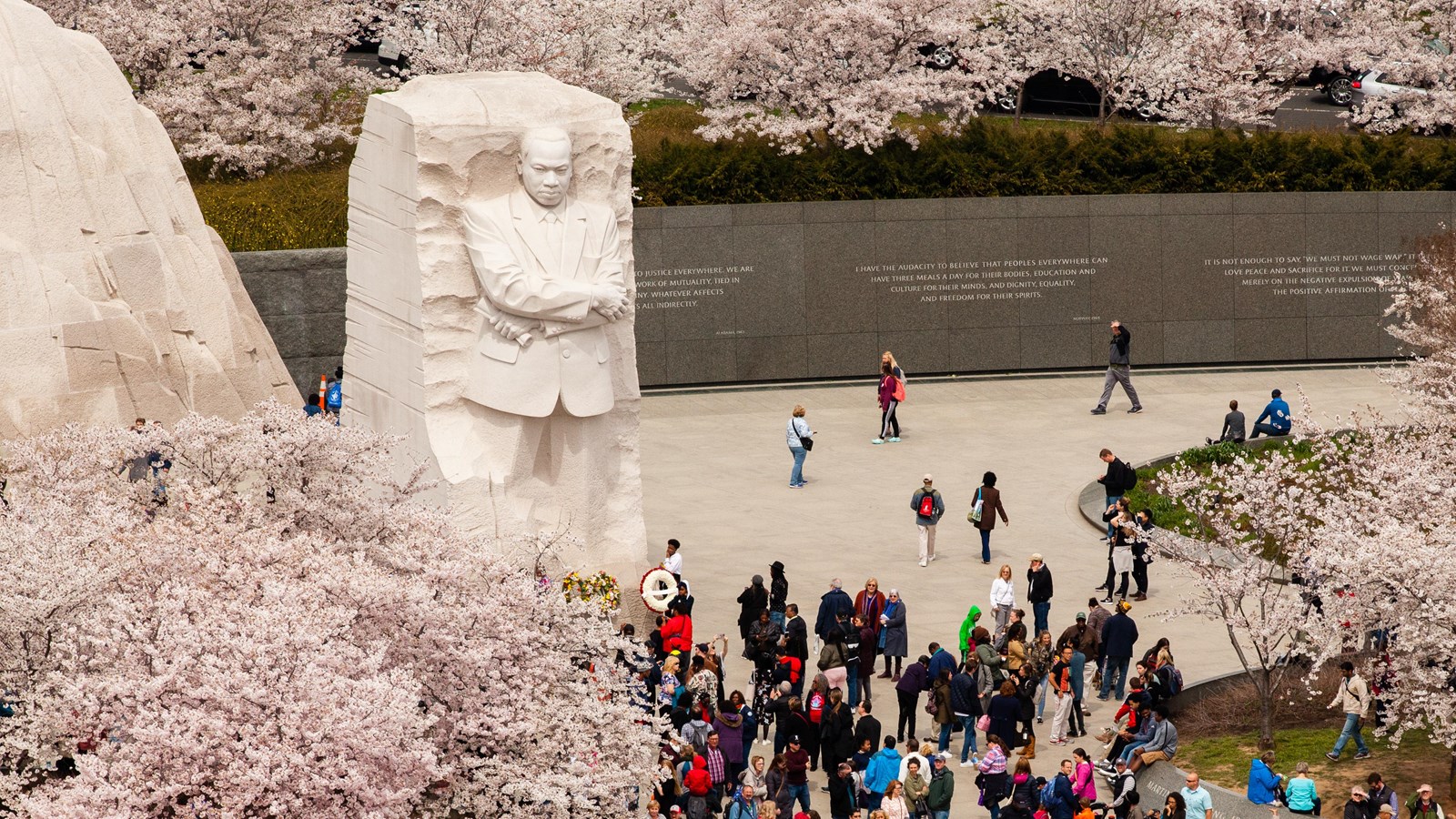 Open plaza with a tall statue of a man with people looking at flowering trees