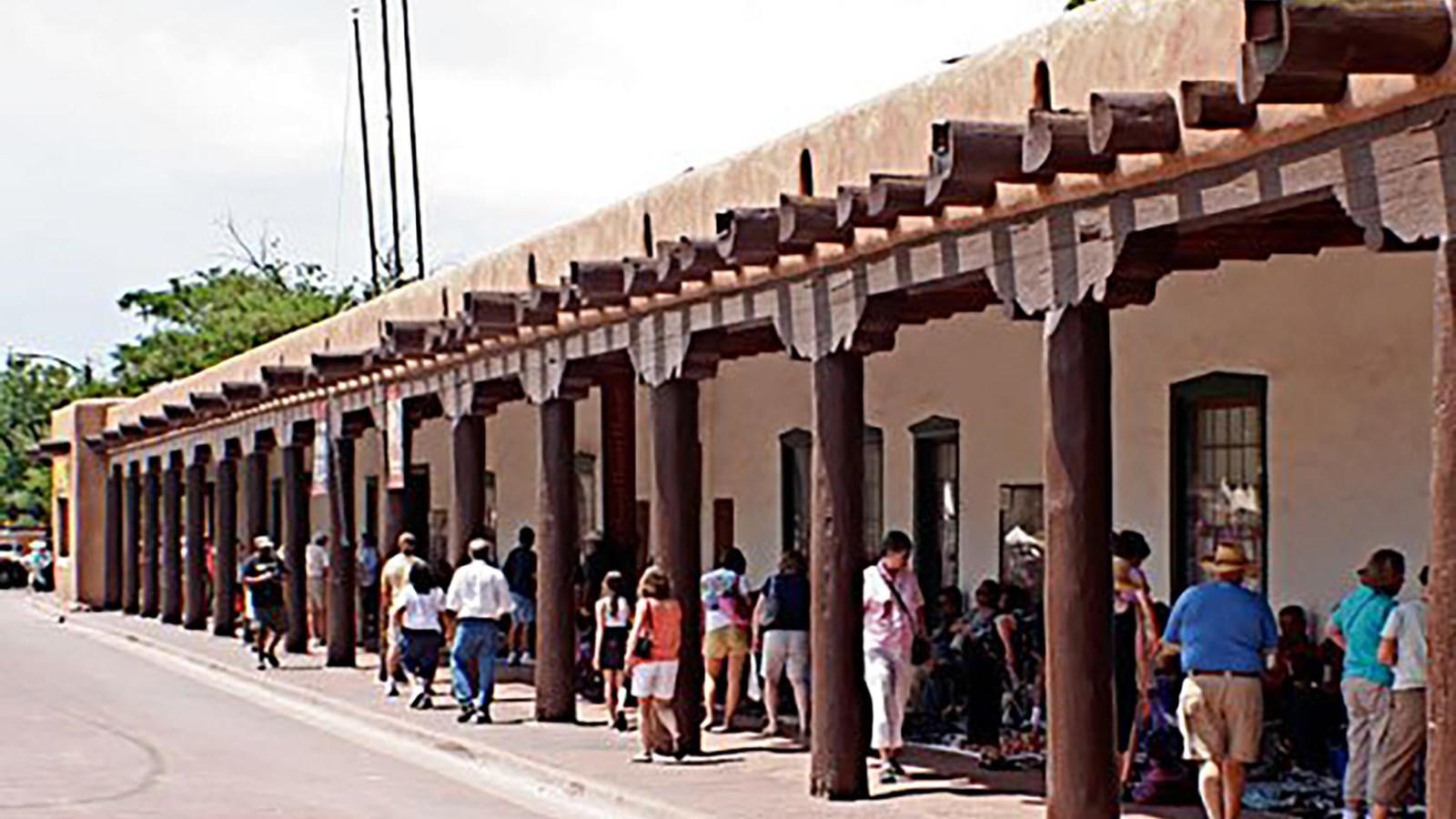A one story adobe building with people walking under the covered hacienda.