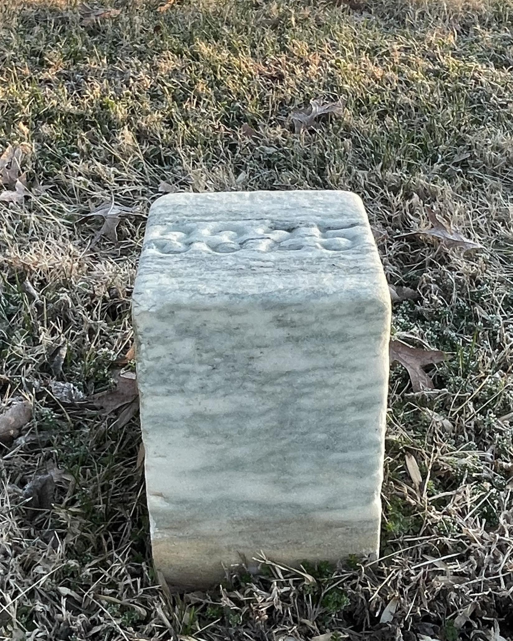 Short, cube shaped marble headstone with a number on the top representing an unknown grave.