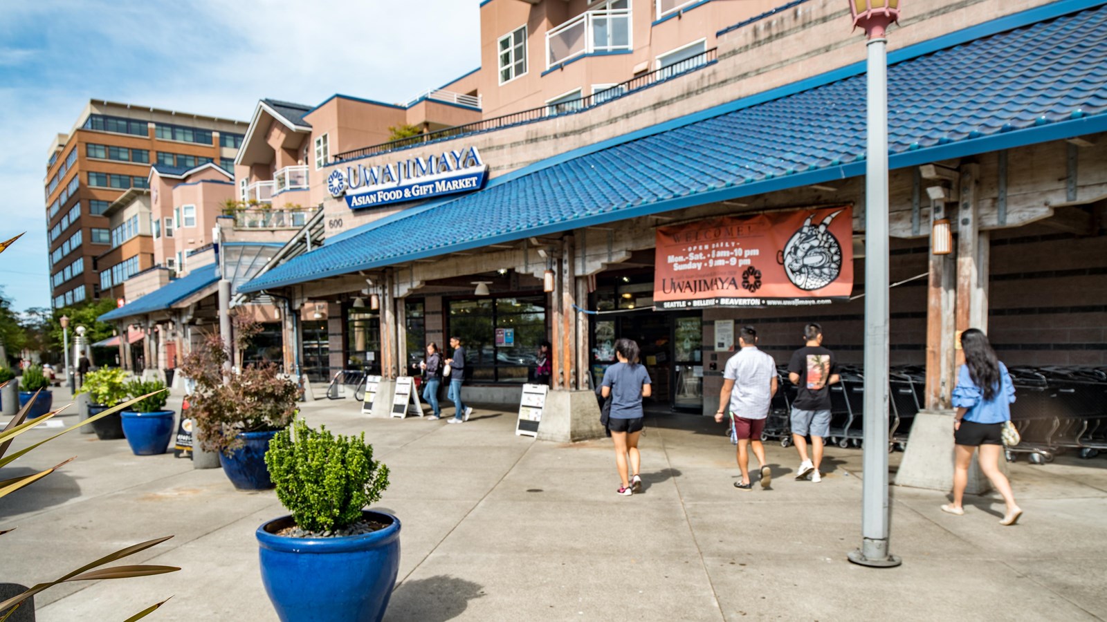 Several people are walking towards the main entrance, passing by bright blue planters with shrubbery
