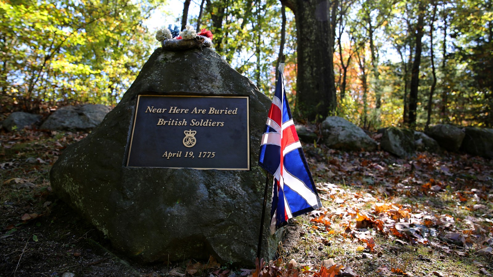 A stone grave marker for British soldiers sits on a small wooded knoll. There are flowers on top