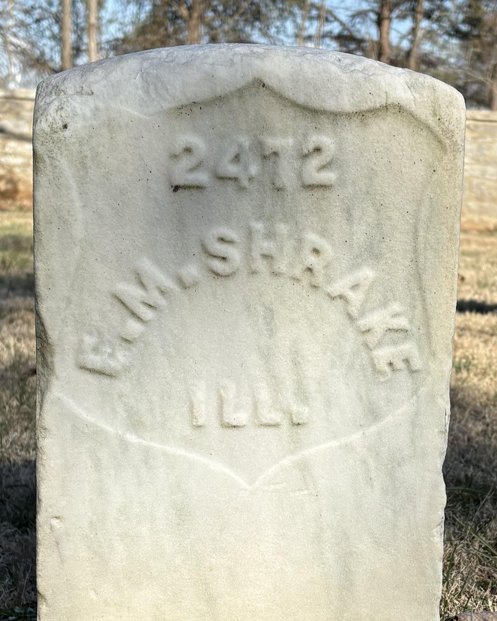 Marble headstone backed by a stone wall. 