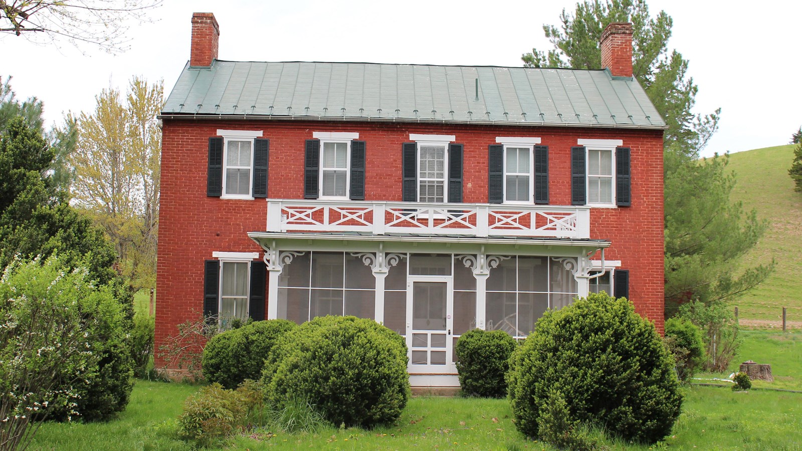 An antebellum Georgian style house has a red brick façade and white columns supporting a balcony.