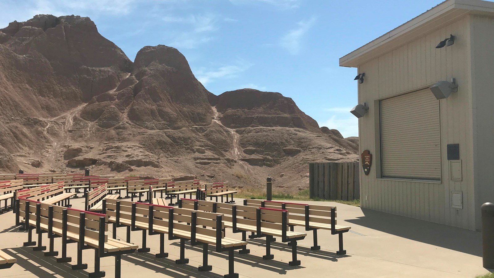 Rectangular tan building facing several dozen rows of benches under blue sky.