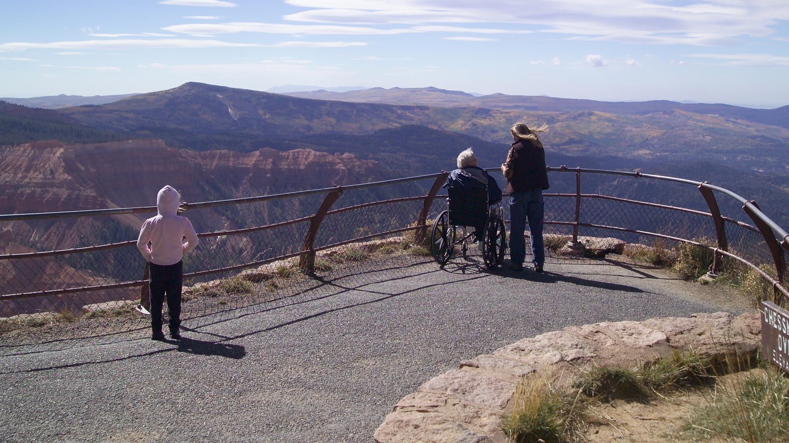 Three people look over railings to rock formations in the distance.