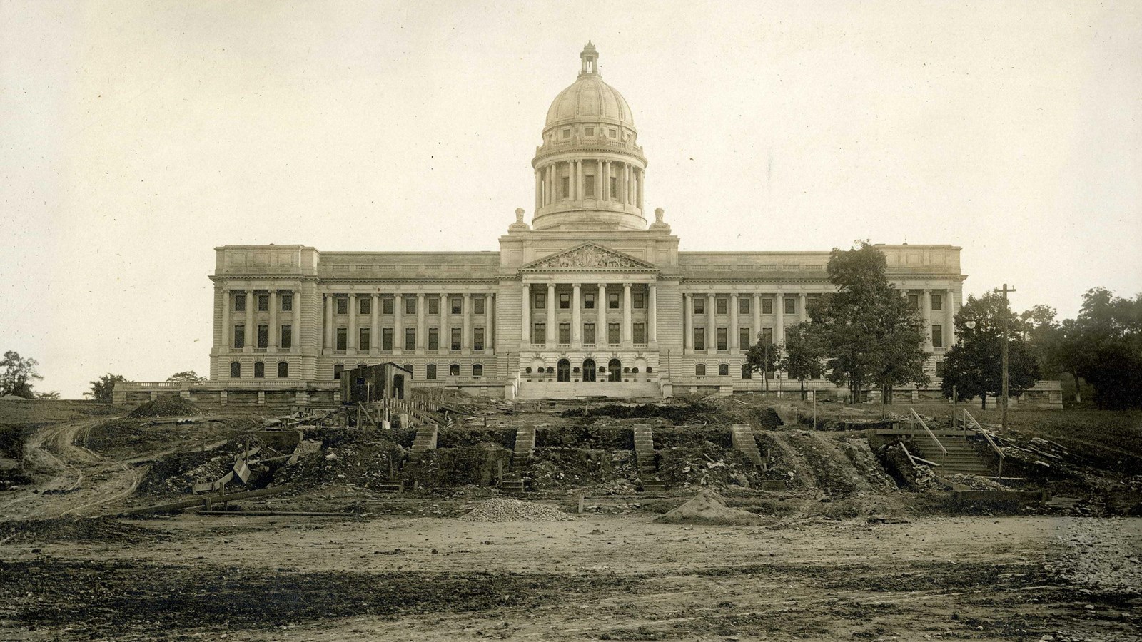 Black and white of large white building with dome with dirt hill leading up and stairs