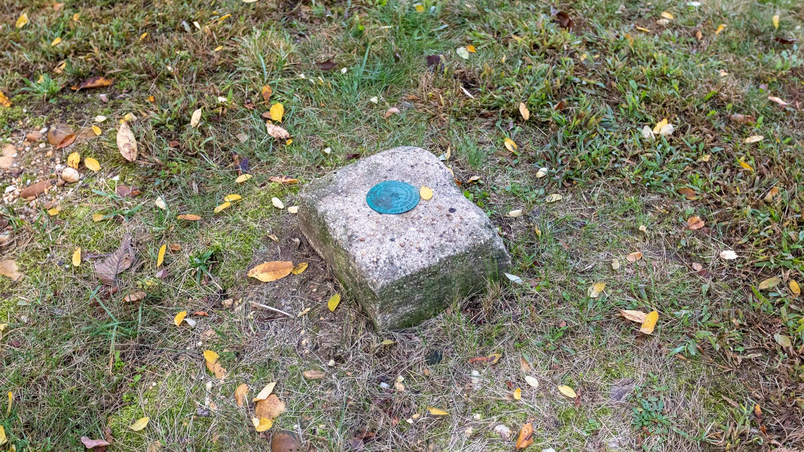 A flag pole stand surrounded by grass.