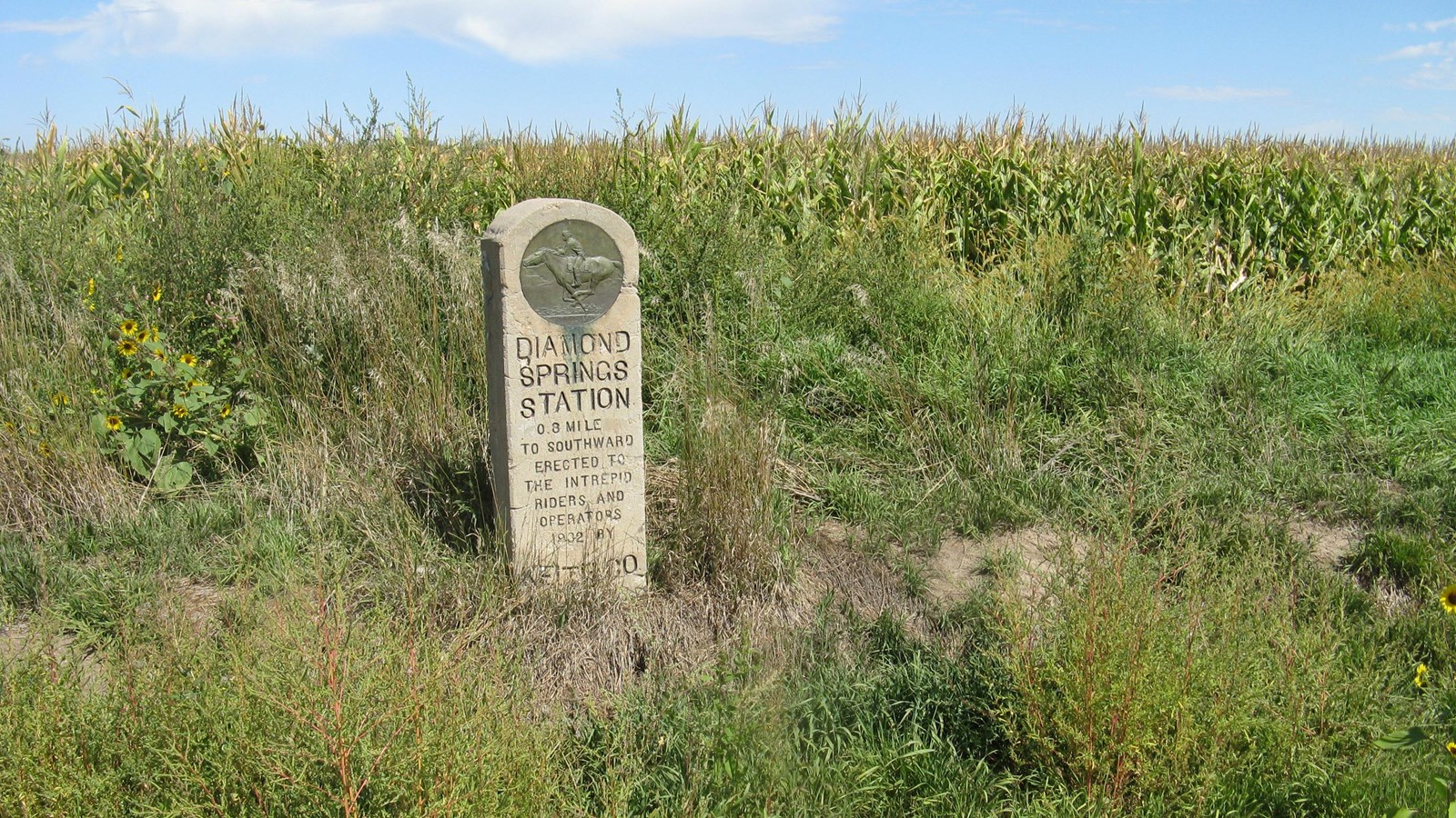 A tall concrete Pony Express monument stands above a grassy ditch.