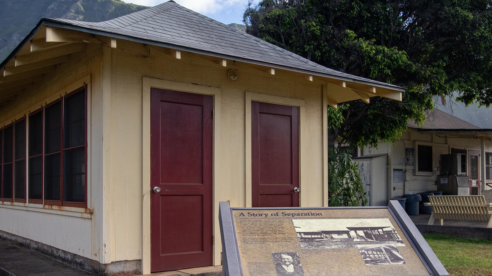 A wayside with information in front of a narrow building with two red doors separated by one foot.