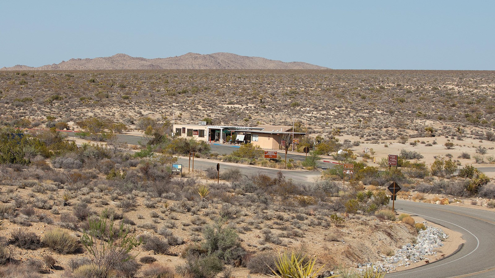A road leads to a tan building sits in an open desert landscape