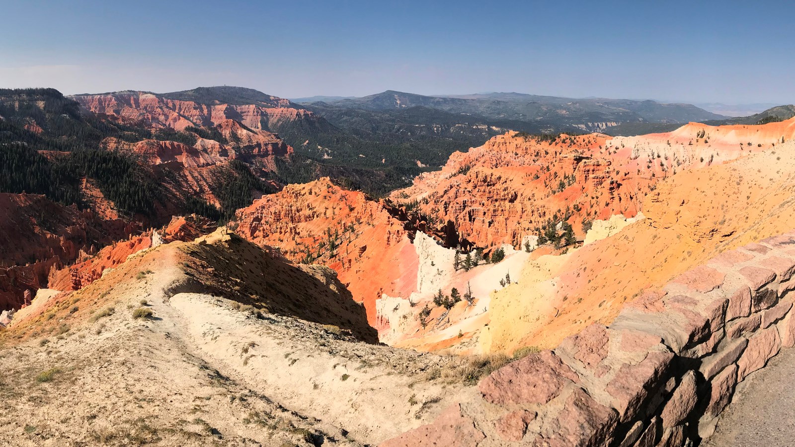 A short stone wall stands on the rim of a large geologic amphitheater extending into the distance.