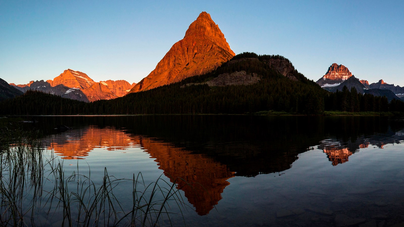 Golden morning light hit a mountain, which is reflected onto a smooth lake.