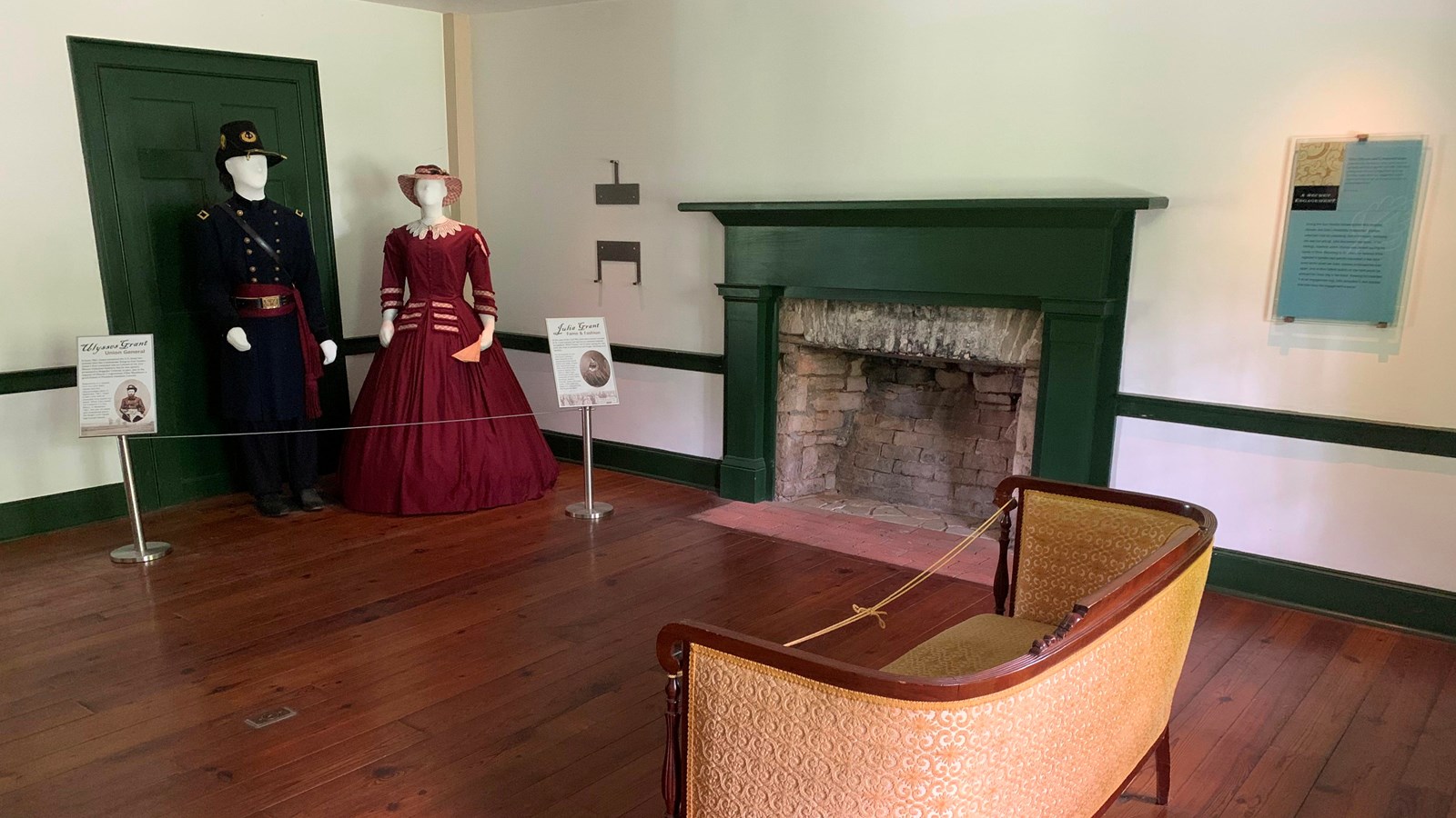 Two mannequins dressed in historic clothing stand in a room next to a fireplace and furniture