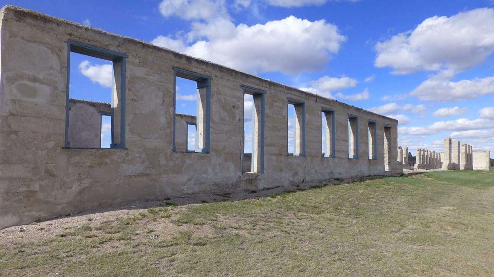 A row of cement walls and pillars sitting on a grassy field.  