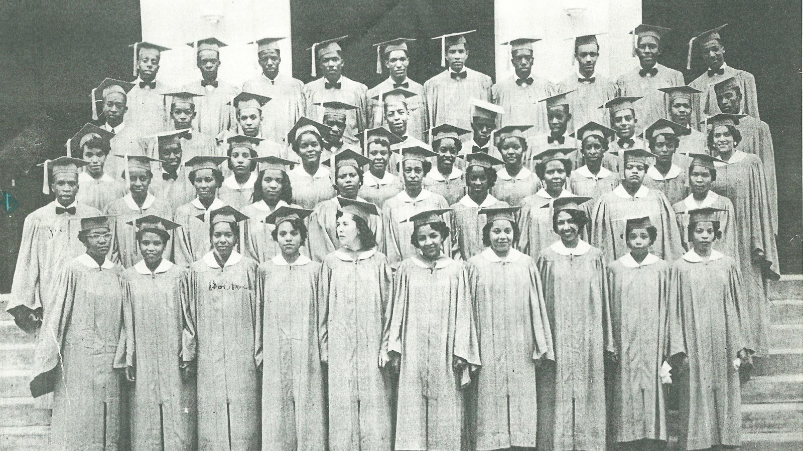 Black and white photo of graduating students lined up in rows on the steps of a building. 