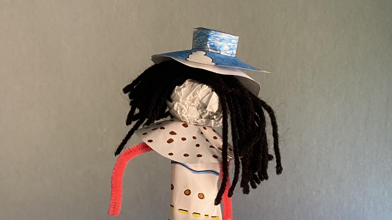 Paper doll with orange arms and blue hat.