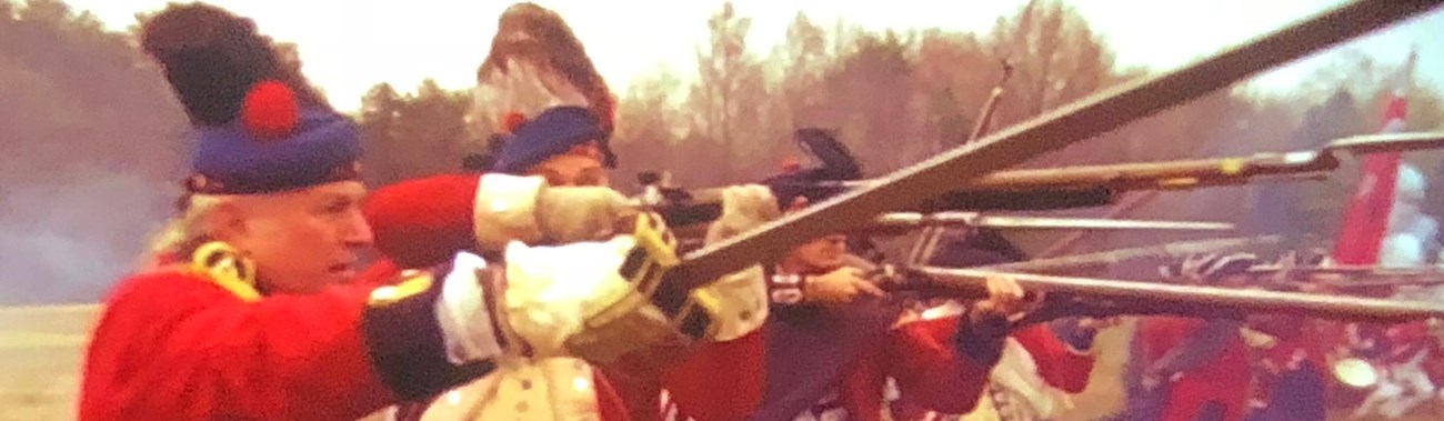 Reenactors portraying Scottish Highlander soldiers raise swords and muskets for battle.