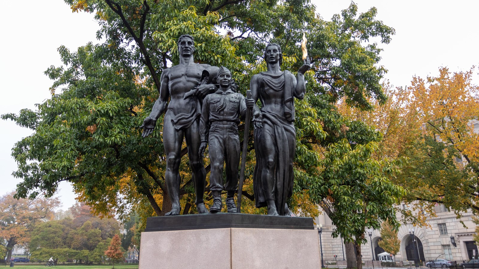 A monument depicting a man, a boy scout, and a woman. A small circular pool is in front.