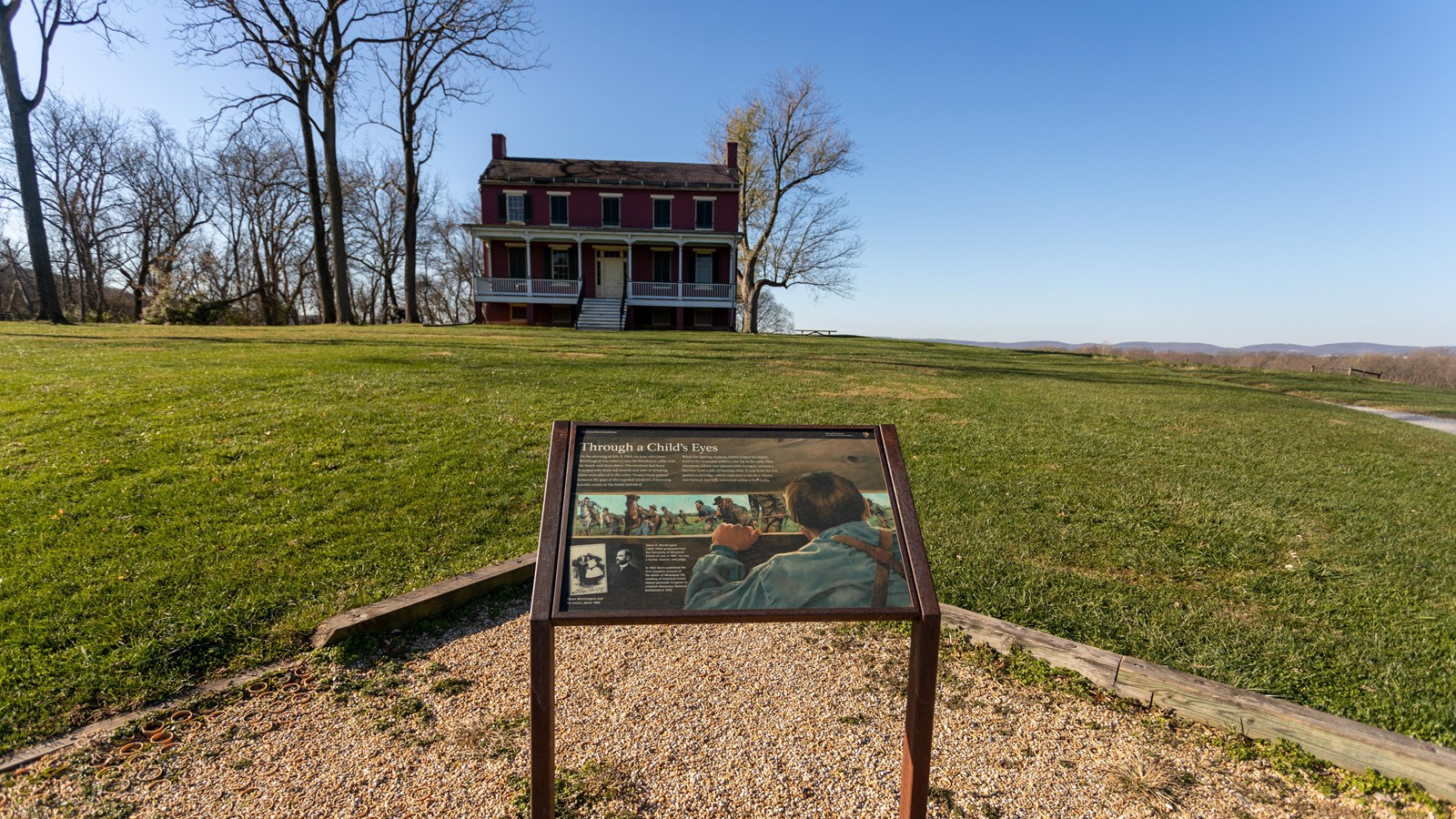A informational panel in front of a grassy field and a house.
