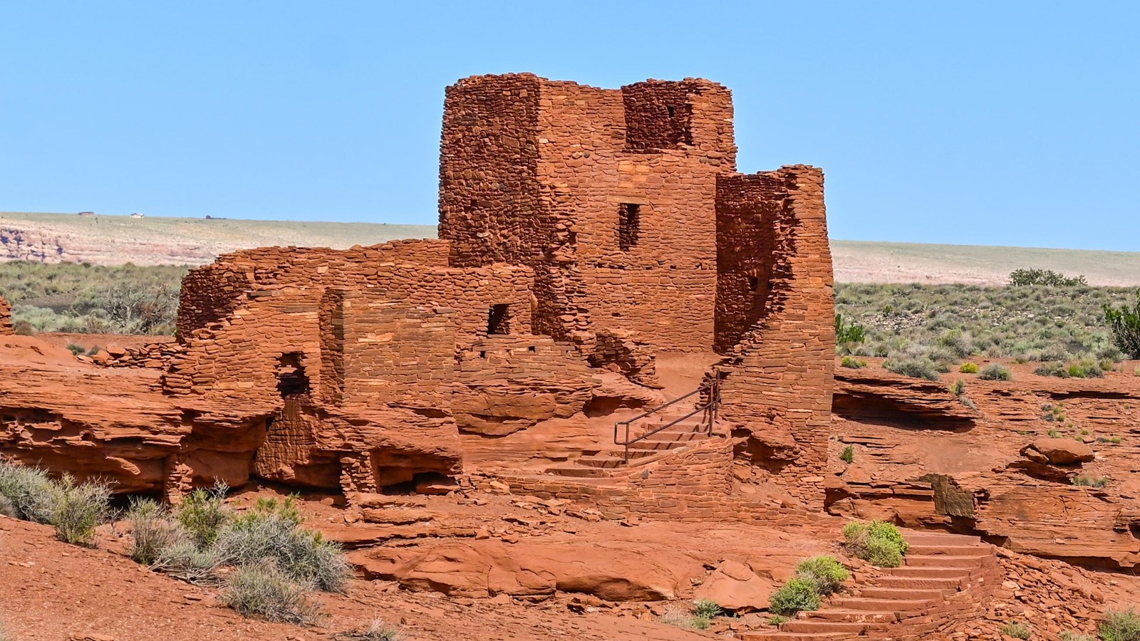 A red sandstone pueblo with a three-story tower sits in a desert landscape against a blue sky