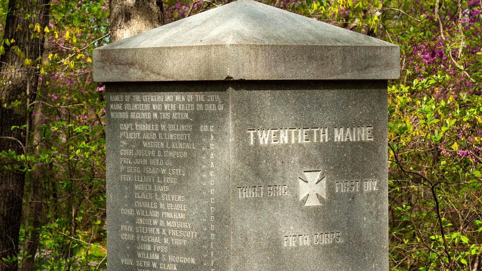 A stone monument sits on a rock near a wooded area.
