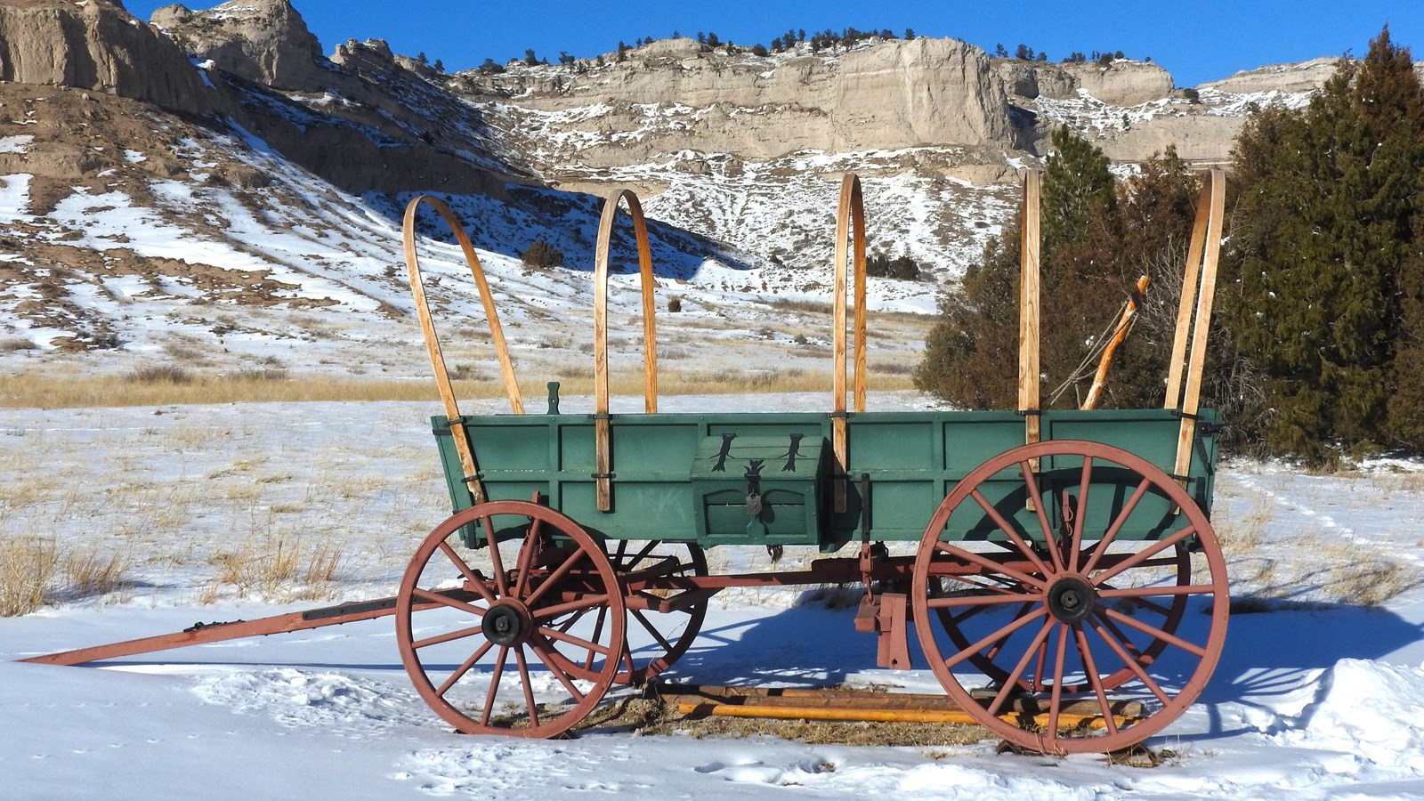 A 1800s-style wagon is painted green with red wheels. Bows are visible but do not hold a cover. 