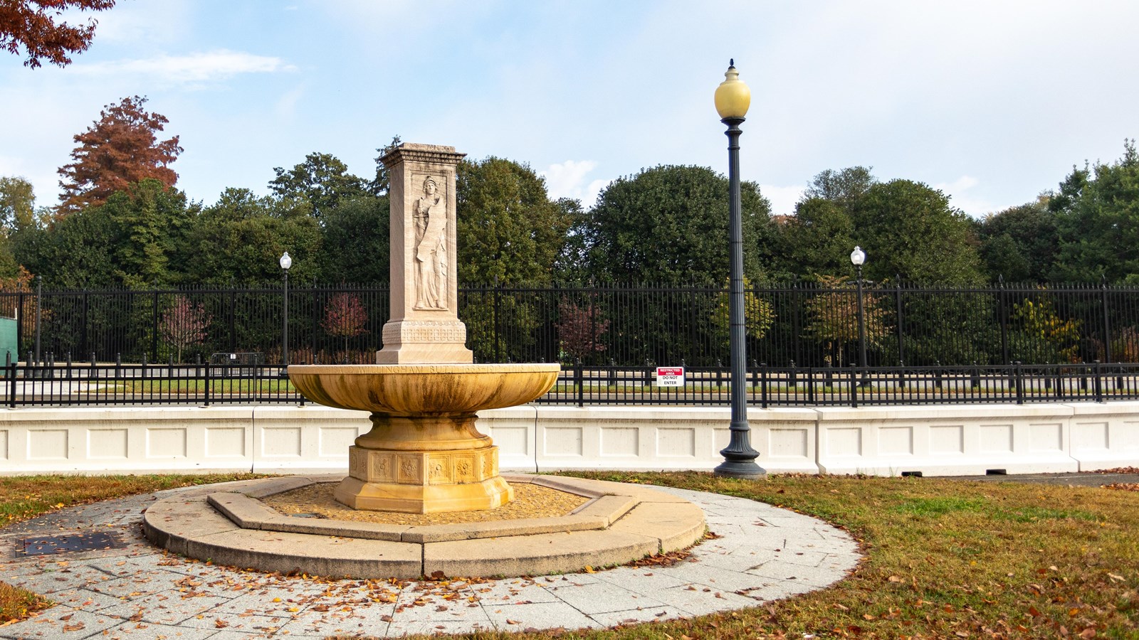 A circular fountain with a rectangular stone sculpture depicting Francis Davis Millet in the middle.