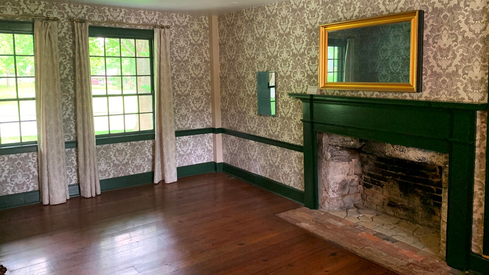 Victorian-style wallpaper coats a room with a fireplace with a mirror above it.