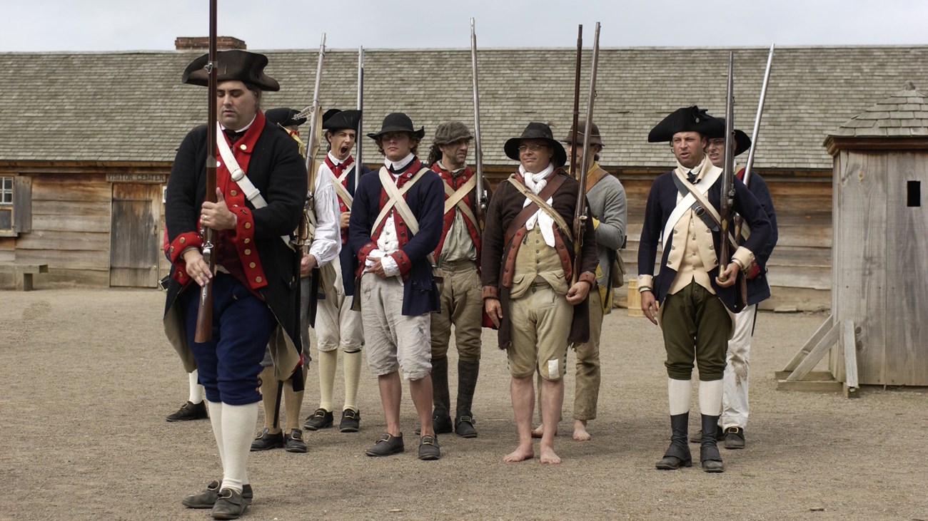 A small company of about 24 soldiers stand in formation. They all have different uniforms.