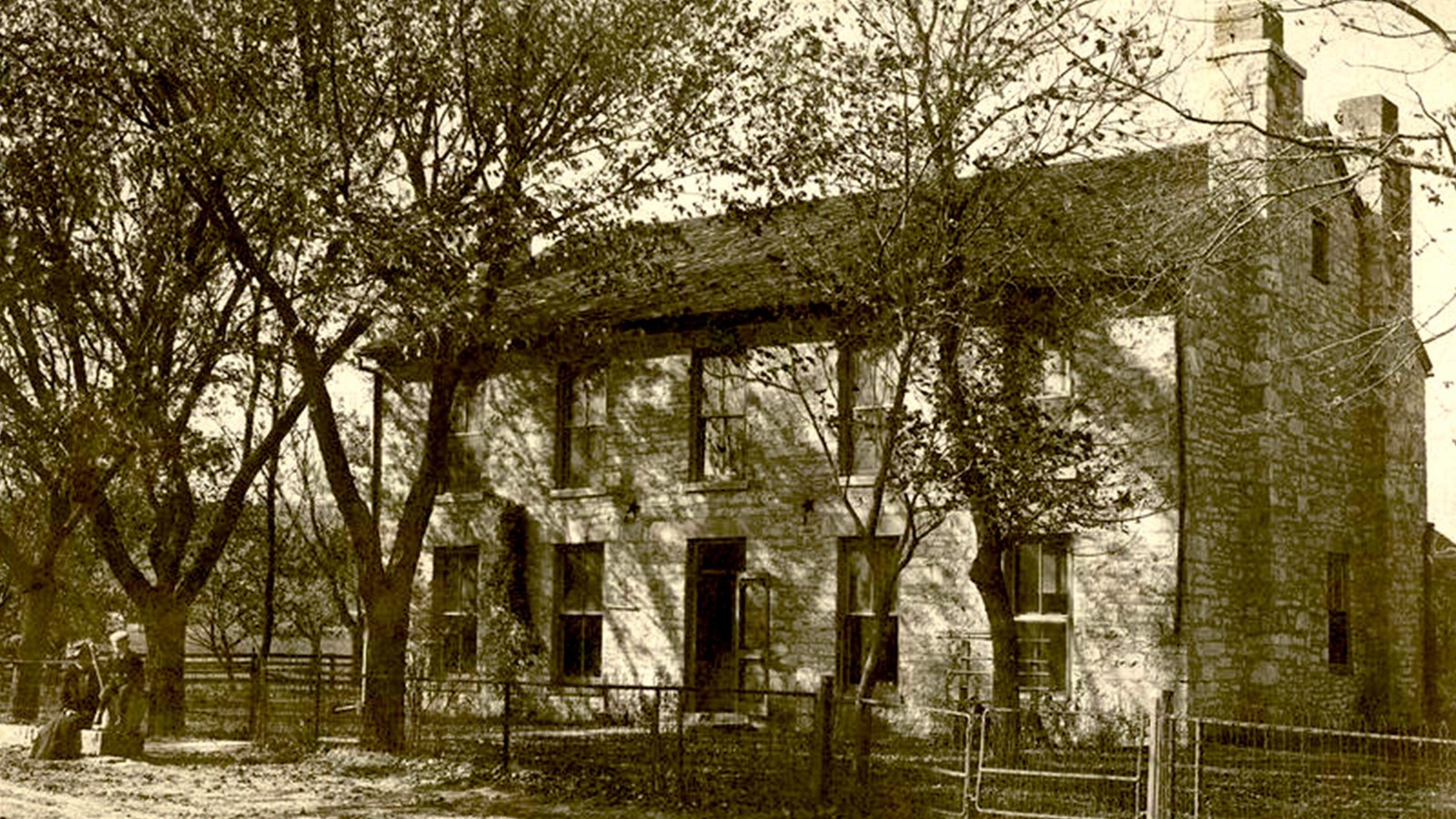 two-story stone house with the chimneys rising at each end. There is a central doorway with windows.