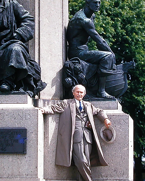 Two bronze statue of soldiers at rest in front stands a man in a tan suit holding a hat