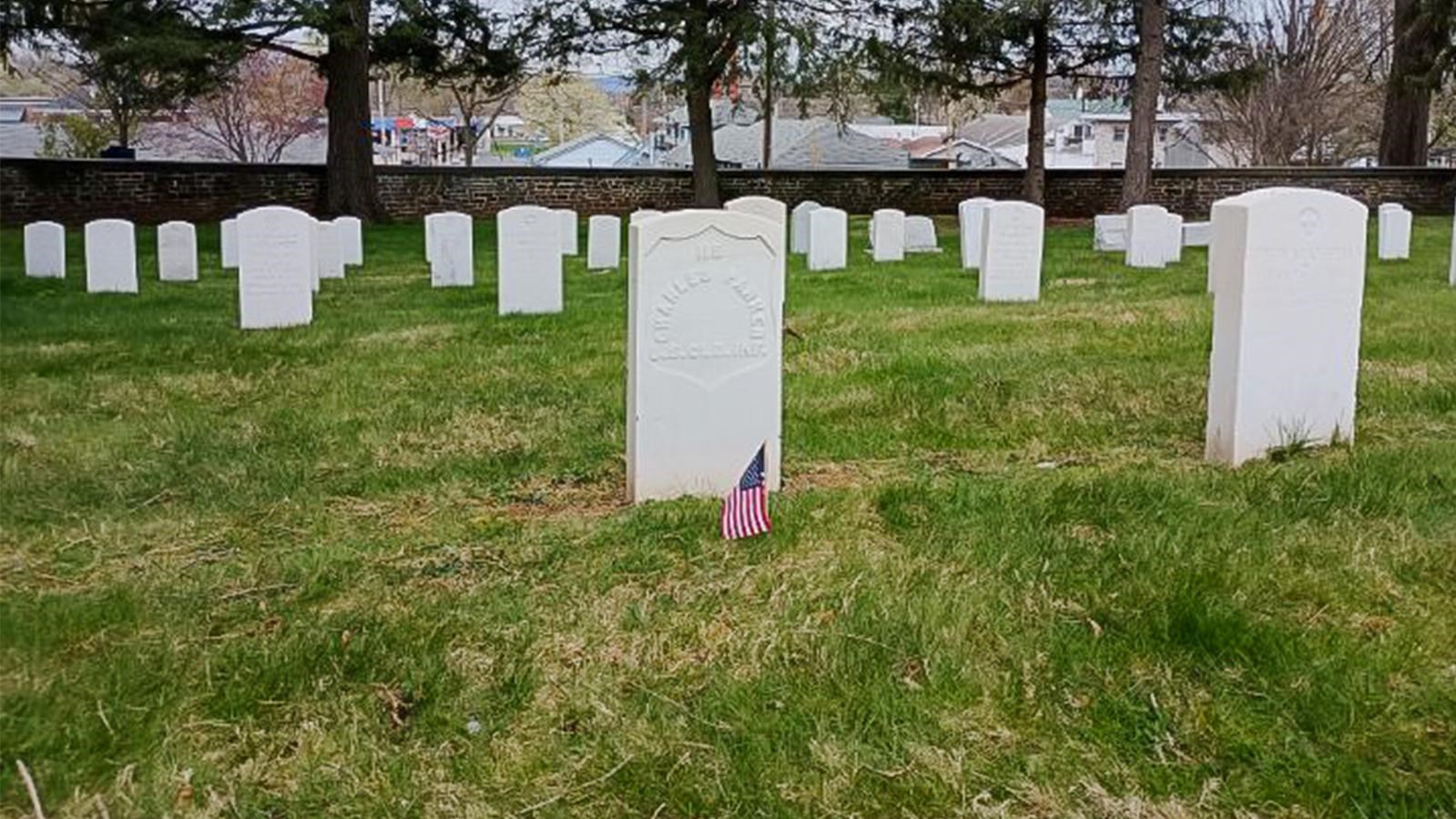 A white marble gravestone with small United State flags surrounded by other white headstonestones.